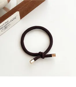 Close-up of a dark brown elastic braided hair tie with a gold metal knot finish