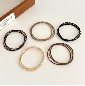 Détail de cinq chouchous perlés aux tons terre avec accents dorés sur fond minimaliste