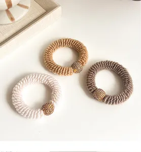 Detail of three knitted spiral hair ties in beige and coffee with rhinestone gold beads