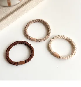 Detailed view of three braided elastic hair ties in earthy tones on a minimalist tray