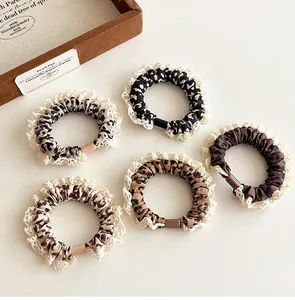 Detailed set of leopard print hair scrunchies with white lace edges on beige background