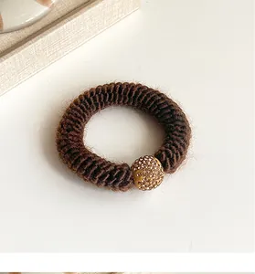Detail of coffee brown braided yarn hair tie featuring a sparkling rhinestone gold bead
