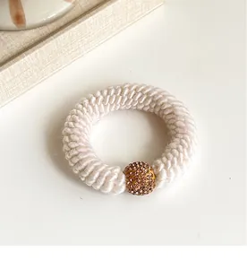Macro shot of beige knitted hair tie with thick ribbed texture and sparkling rhinestone bead
