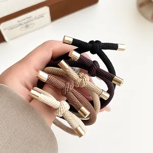Five elastic knotted hair ties in earth tones with gold metal tips held by hand