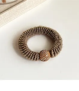 Close-up of brown knitted elastic hair tie featuring a golden rhinestone ball detail