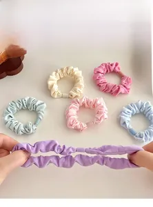 Detail display of five pastel fabric scrunchies showing strong elastic stretch and texture