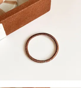 Détail d'un élastique à cheveux marron avec texture pailletée dans une boîte