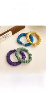 Détail de quatre chouchous en velours colorés avec fermoir mat sur surface blanche