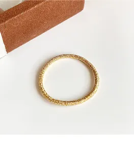 Détail macro d'un élastique à cheveux doré brillant avec texture métallique sur blanc
