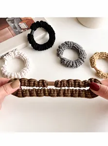 Detail of hand stretching thick elastic hair ties in neutral earth tones