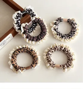 Close-up of leopard print scrunchies with white lace edges on a cream surface
