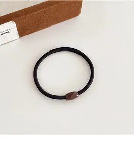 Detail van een elastische zwarte haarelastiek met een gepolijste donkerbruine cilinderkraal