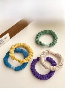 Détail de cinq chouchous en velours colorés avec boucles mates sur fond neutre uni