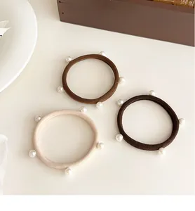 Dettaglio di tre elastici per capelli con perle in beige, marrone e caffè