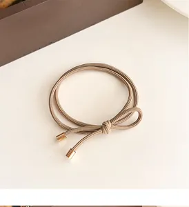 Detail of coffee brown bow hair tie featuring multi-strand elastic rope and gold metal tips