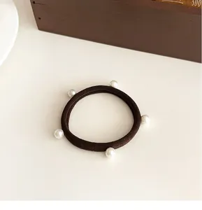 Dettaglio dell'elastico per capelli caffè con cinque eleganti perle bianche