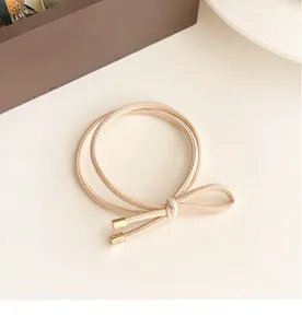 Detail of high-elastic beige bow hair tie with elegant gold cylindrical metal buckles