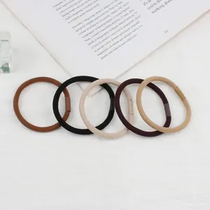 Five elastic hair ties in earth tones arranged on a white textured background with a book