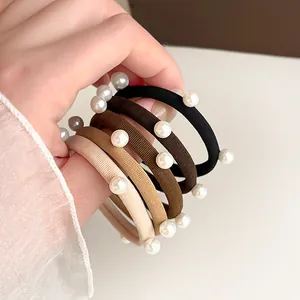 Set da cinque elastici per capelli con perle color caffè latte tenuti in mano