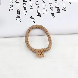 Detail eines gewebten Khaki-Haargummis mit braunem Smiley-Gesicht-Lederaufnäher