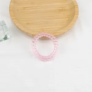 Dettaglio dell'elastico a spirale rosa pallido su vassoio in legno e trama bianca