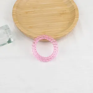Dettaglio di un elastico a spirale rosa in resina traslucida su un vassoio di legno