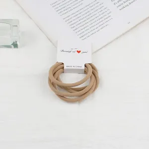 Close-up of four khaki elastic hair ties on a white display card with soft lighting