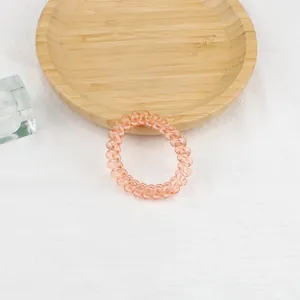 Macro di un elastico per capelli a spirale arancione-rosa su un vassoio di legno minimale