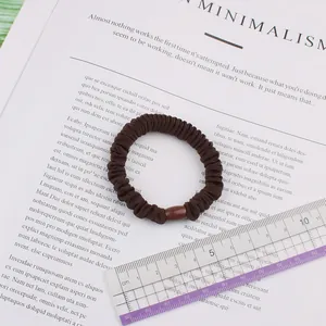 Detail of dark brown scrunchie with bead decoration next to a ruler for size