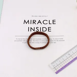 Elastic brown braided hair tie with a 5cm diameter on a clean aesthetic background