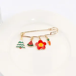 Détail d'une broche épingle dorée avec breloques émaillées de Noël sur une assiette blanche