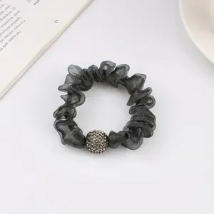 Detail of dark grey mesh scrunchie with sparkling rhinestone ball charm on white desk
