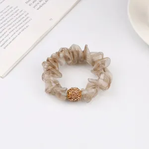 Close-up of champagne mesh scrunchie with sparkling rhinestone ball and textured fabric