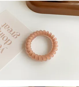 Detail view of a matte pale pink spiral hair tie on a decorative aesthetic background