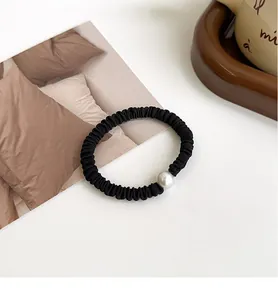 Detalle de un coletero negro plisado con perla blanca en un ambiente de mesa
