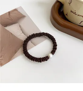 Detalle de coletero marrón elástico con perla blanca para peinados de coleta alta elegante