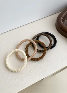 Nahaufnahme von vier spiralförmigen Haargummis in Creme- und Kaffeetönen auf weißem Grund
