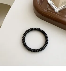 Detailansicht eines schwarzen Spiralhaargummis mit glänzender Oberfläche auf hellem Grund