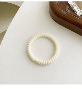 Makro-Detail eines hochelastischen cremefarbenen Spiral-Haargummis auf minimalistischem Grund