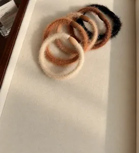 Detailed view of five assorted warm-toned plush hair scrunchies on a white jewelry tray