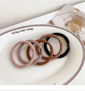Detail of five thick elastic hair ties in earth tones on a white ceramic plate