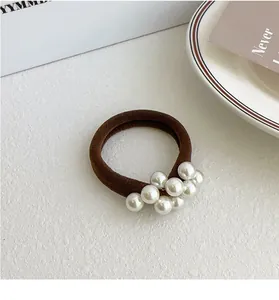Detail van een bruine elastische haarknoop met witte parels op een minimalistische basis