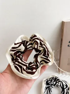 Detailed view of zebra print scrunchie with satin ribbon detail and Change text embroidery