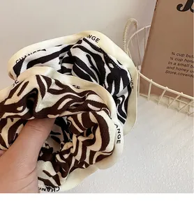 Close-up of zebra pattern fabric hair scrunchies with white edge ribbon and text detail