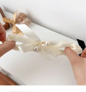Detail showing high elasticity of the off-white mesh hair scrunchie with a satin bow and pearls