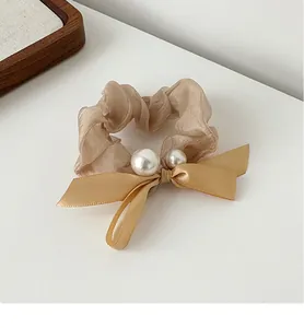 Close-up of champagne organza scrunchie with satin bow and white faux pearl accents