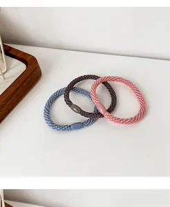 Close-up of three woven elastic hair bands in blue, grey, and pink on white surface