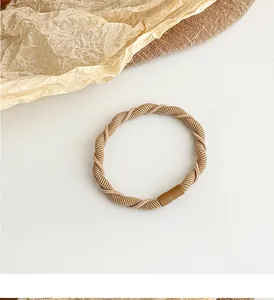 Macro view of braided khaki hair tie with smooth brown joint on textured fabric