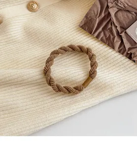 Dettaglio di un elastico per capelli intrecciato marrone caffè su tessuto beige