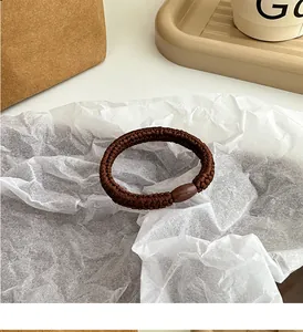 Detail eines dunkelbraunen geflochtenen Haargummis mit glatter Perle auf Seidenpapier